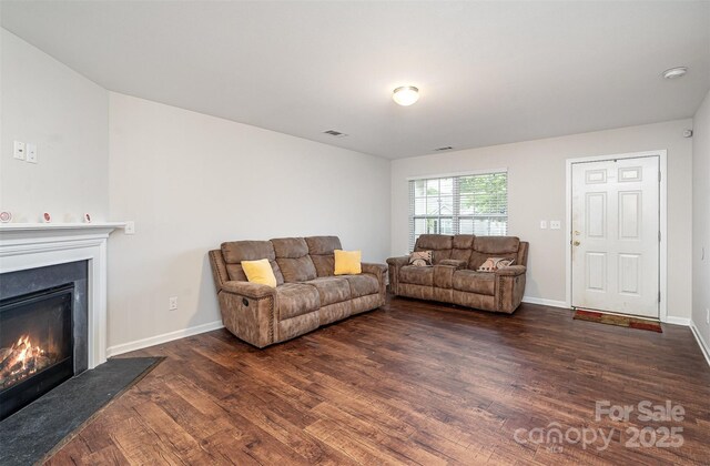 living room featuring a glass covered fireplace, dark wood finished floors, and baseboards