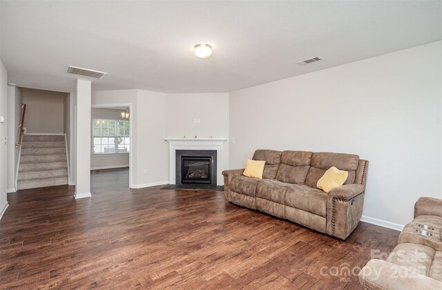 living room with baseboards, dark wood-type flooring, stairs, and a fireplace with flush hearth