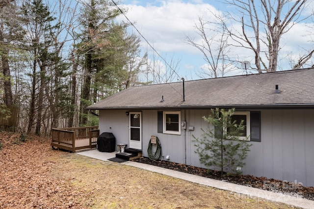 back of house featuring roof with shingles and a wooden deck