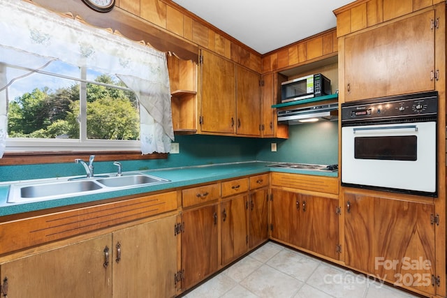 kitchen with white oven, a sink, brown cabinetry, stainless steel cooktop, and ornamental molding