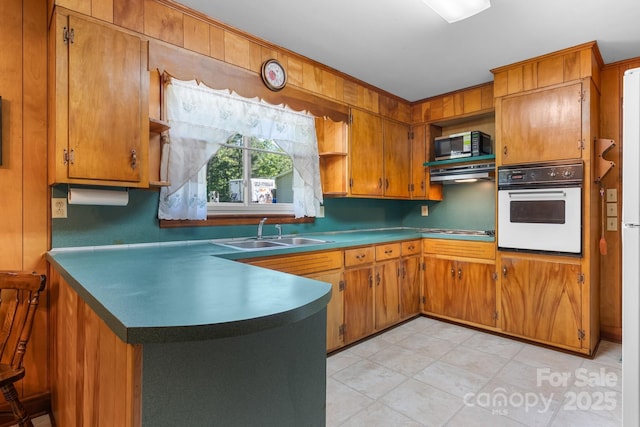 kitchen with white oven, a sink, brown cabinetry, and black microwave