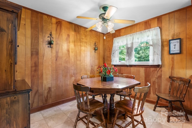 dining area with a ceiling fan, wood walls, and baseboards
