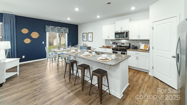 kitchen featuring stainless steel appliances, a breakfast bar area, a sink, light stone countertops, and white cabinets