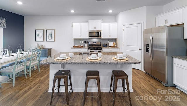 kitchen featuring stainless steel appliances, a kitchen breakfast bar, light stone counters, white cabinetry, and recessed lighting