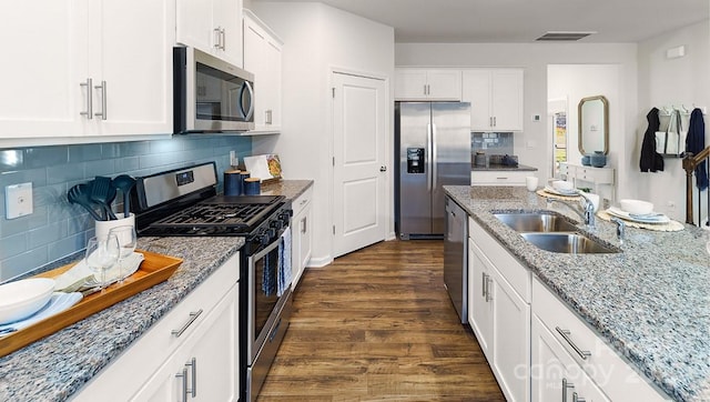 kitchen featuring appliances with stainless steel finishes, a sink, dark wood-type flooring, light stone counters, and white cabinetry