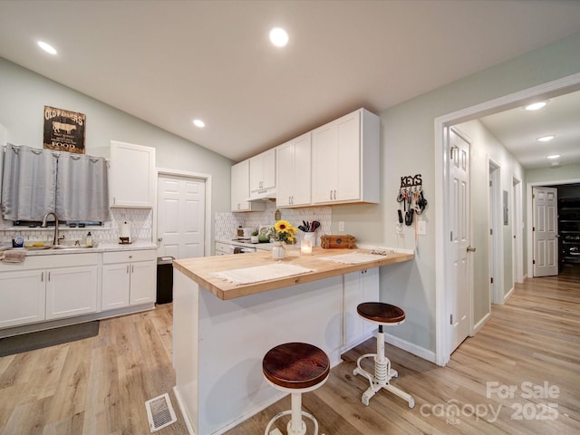 kitchen featuring a sink, a breakfast bar, white cabinets, light wood-style floors, and recessed lighting