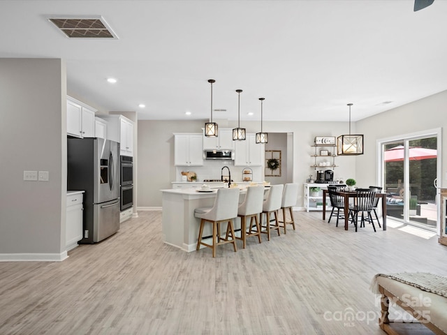 5013 Hamilton Mill Dr, Waxhaw, NC 28173 - kitchen featuring appliances with stainless steel finishes, light wood-type flooring, a breakfast bar, white cabinetry, and light countertops