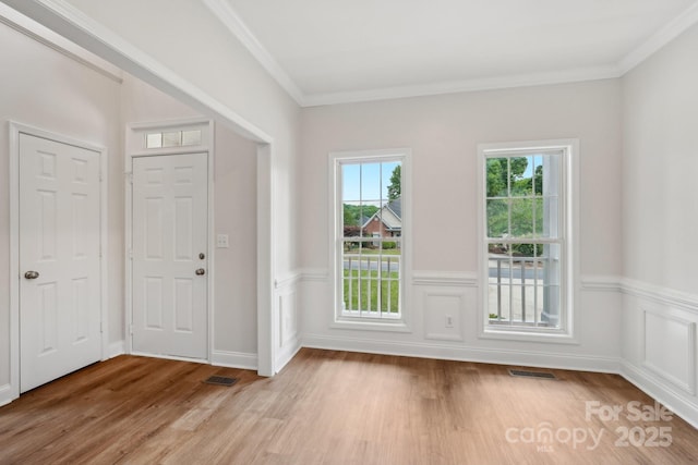 entryway featuring light wood-type flooring, crown molding, and a wainscoted wall