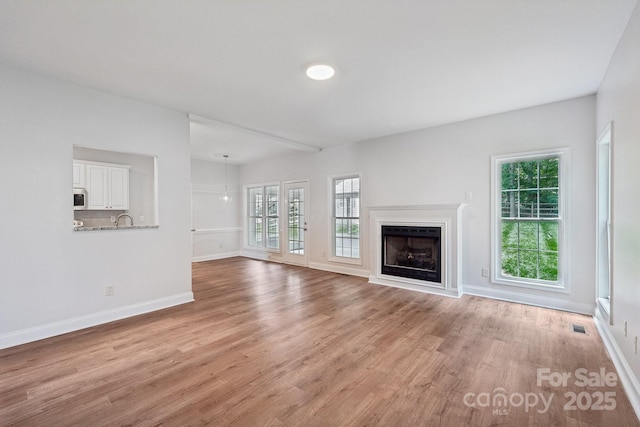 unfurnished living room featuring light wood-style floors, baseboards, a fireplace, and a sink