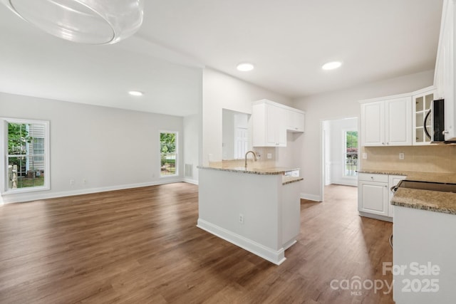kitchen with white cabinetry, light stone counters, wood finished floors, glass insert cabinets, and recessed lighting