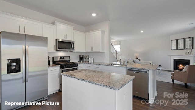 kitchen featuring stainless steel appliances, a peninsula, open floor plan, a sink, and light stone countertops