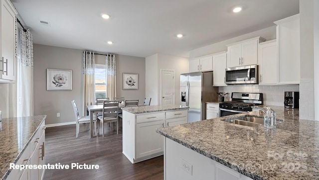 kitchen with appliances with stainless steel finishes, a sink, dark wood finished floors, a center island, and light stone counters