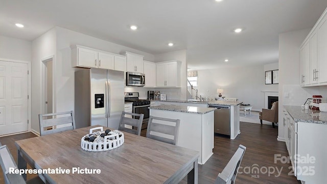 kitchen with stainless steel appliances, a kitchen island, a peninsula, a fireplace, and white cabinetry