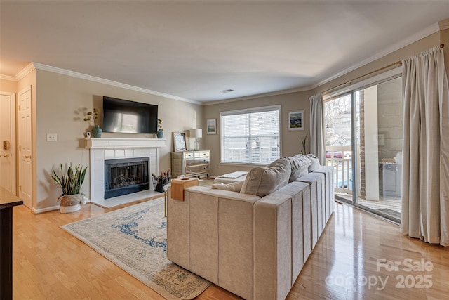 living room featuring ornamental molding, light wood-style flooring, a tiled fireplace, and baseboards