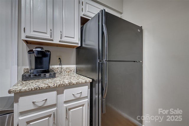 kitchen with freestanding refrigerator, white cabinetry, and light stone countertops