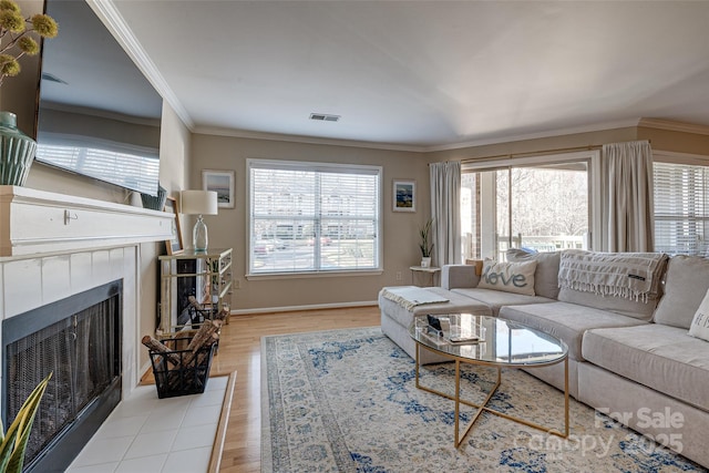 living room featuring wood finished floors, ornamental molding, a tile fireplace, and baseboards