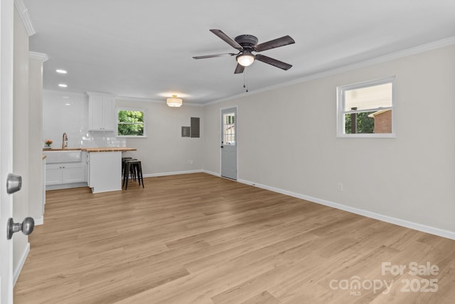 unfurnished living room with crown molding, ceiling fan, baseboards, and light wood finished floors