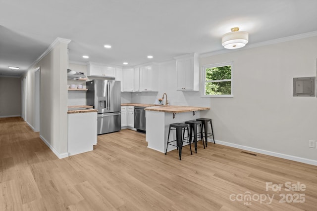 kitchen featuring appliances with stainless steel finishes, a breakfast bar area, crown molding, a peninsula, and white cabinets