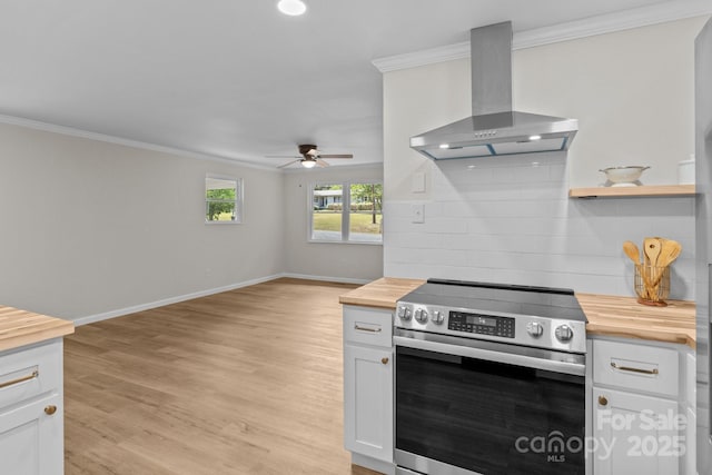 kitchen with wood counters, stainless steel electric stove, wall chimney exhaust hood, crown molding, and ceiling fan