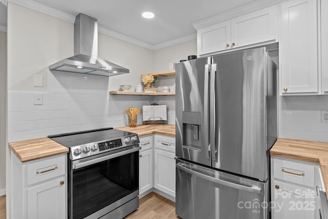 kitchen with wooden counters, appliances with stainless steel finishes, wall chimney range hood, crown molding, and light wood finished floors