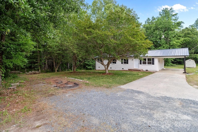 single story home with concrete driveway, a carport, a front lawn, a storage unit, and metal roof