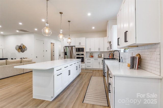 kitchen with stainless steel appliances, a center island, backsplash, light wood-style flooring, and light countertops