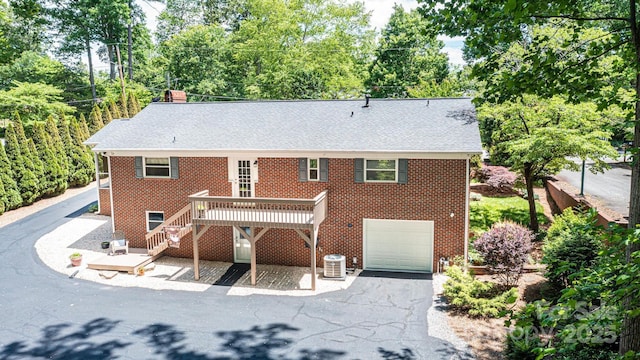 rear view of house with stairs, brick siding, an attached garage, asphalt driveway, and a wooden deck