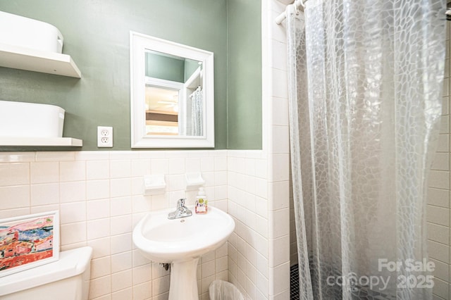 full bathroom featuring toilet, tile walls, curtained shower, a wainscoted wall, and a sink