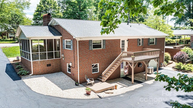 back of house with a sunroom, central AC unit, roof with shingles, brick siding, and a deck