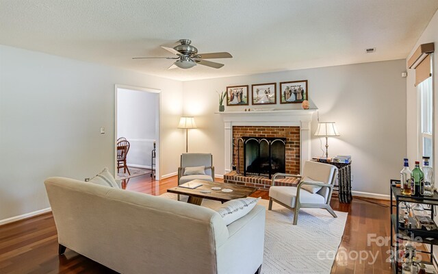living room with ceiling fan, a brick fireplace, wood finished floors, and baseboards