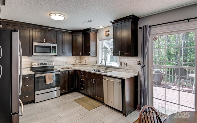 kitchen featuring appliances with stainless steel finishes, a sink, decorative backsplash, dark brown cabinetry, and light stone countertops