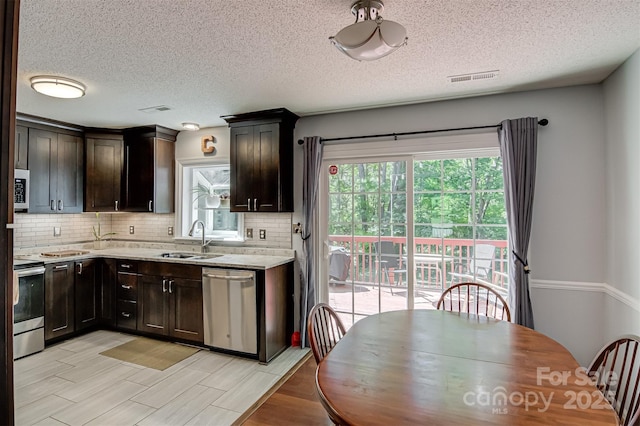 kitchen featuring appliances with stainless steel finishes, a sink, tasteful backsplash, a textured ceiling, and dark brown cabinets
