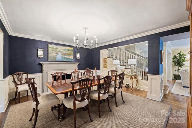 dining room with ornamental molding, wood finished floors, stairway, a chandelier, and a wainscoted wall