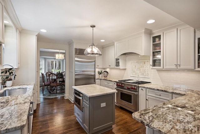kitchen featuring high quality appliances, light stone countertops, white cabinetry, pendant lighting, and ornamental molding