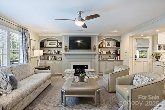 living room featuring ceiling fan, crown molding, recessed lighting, a fireplace, and built in features