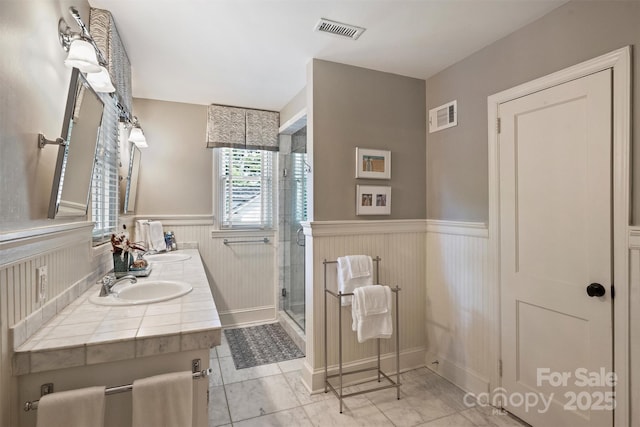 full bath with wainscoting, a stall shower, and double vanity