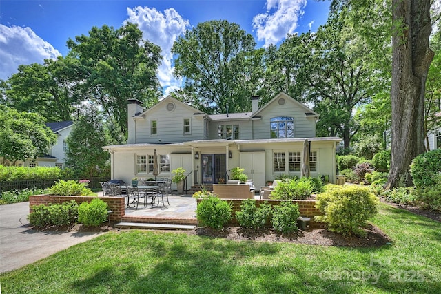 rear view of property with a patio area, a chimney, french doors, and a lawn