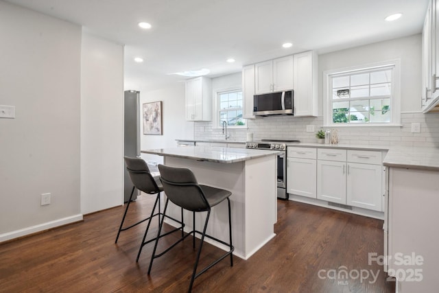 kitchen with stainless steel appliances, a kitchen bar, white cabinetry, decorative backsplash, and recessed lighting