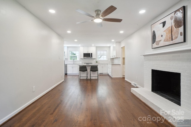 living room featuring a ceiling fan, dark wood-type flooring, a brick fireplace, baseboards, and recessed lighting