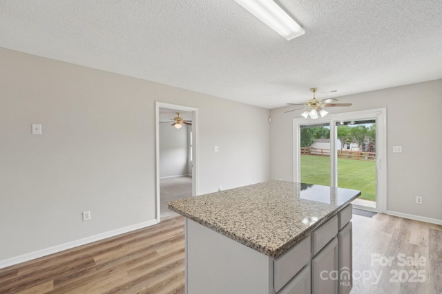 kitchen featuring gray cabinets, light wood-type flooring, a ceiling fan, a textured ceiling, and a kitchen island