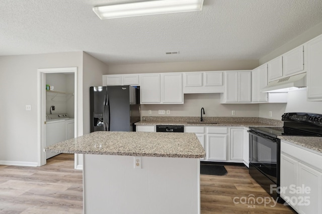 kitchen featuring black appliances, under cabinet range hood, washing machine and dryer, a kitchen island, and a sink
