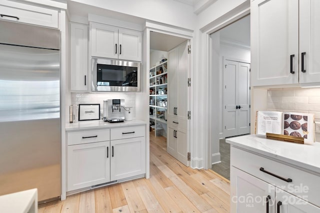 17416 Gillican Overlook Rd, Davidson, NC 28036 - kitchen featuring built in appliances, light wood-style floors, decorative backsplash, white cabinetry, and crown molding