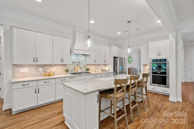 kitchen with appliances with stainless steel finishes, custom range hood, a sink, white cabinets, and light wood-type flooring