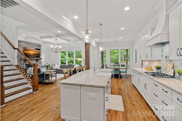 kitchen with stainless steel gas cooktop, premium range hood, recessed lighting, white cabinets, and crown molding