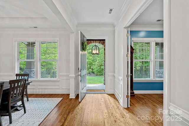doorway featuring wood finished floors, healthy amount of natural light, wainscoting, ornamental molding, and a decorative wall