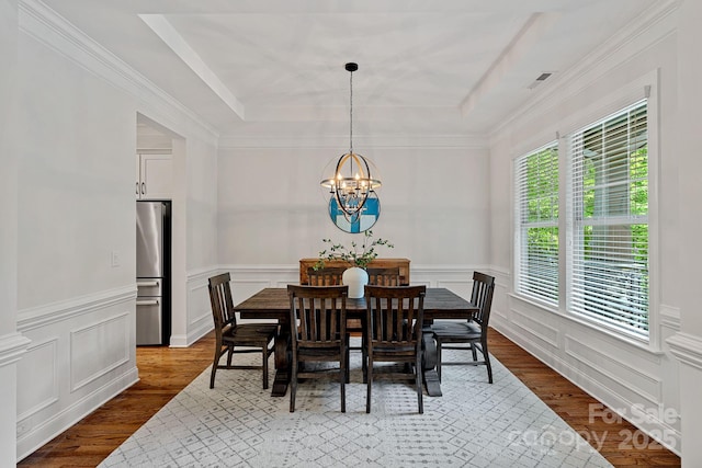dining space with a raised ceiling, a chandelier, wood finished floors, a wainscoted wall, and a decorative wall