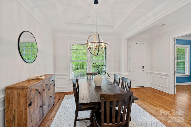 dining space with light wood-type flooring, a chandelier, a tray ceiling, a decorative wall, and a wainscoted wall