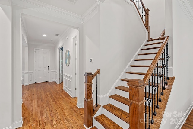 entrance foyer with light wood-style floors, crown molding, stairs, a decorative wall, and wainscoting