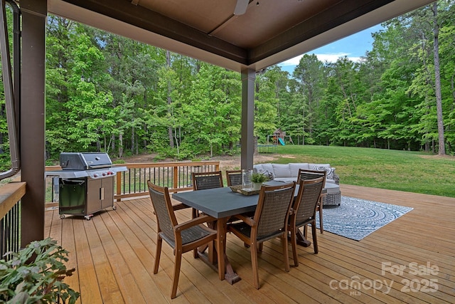 wooden terrace featuring area for grilling, a playground, a lawn, a ceiling fan, and outdoor dining area