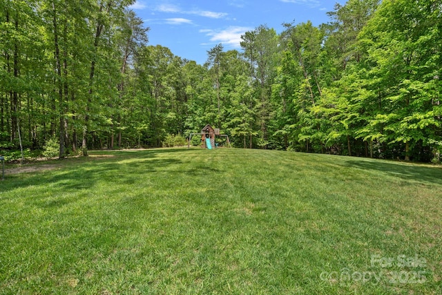 view of green lawn with a playground and a forest view